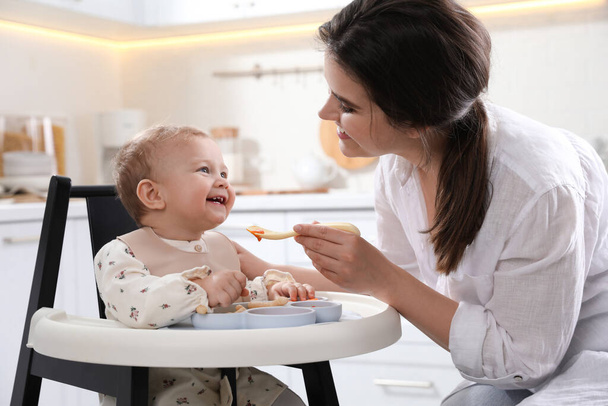 Mother feeding her cute little baby in kitchen - Valokuva, kuva