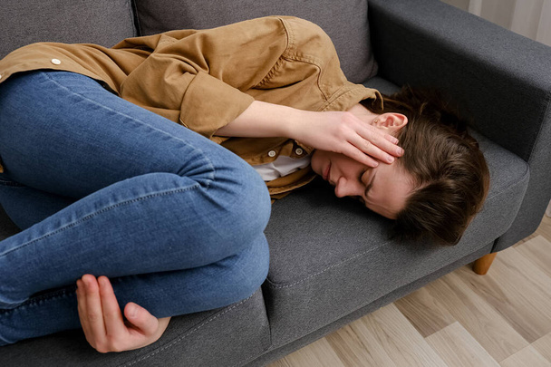 Close up of anxious tired young female lying on sofa feeling doubtful making difficult decision. Nervous unhappy millennial lady suffering from negative thoughts, relationship problems concept - Fotografie, Obrázek