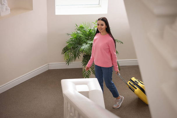 Beautiful young woman with suitcase going up stairs in hotel - Photo, image