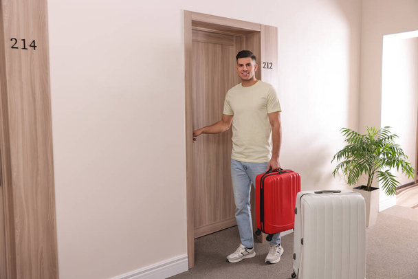 Happy man with suitcase opening door in hotel - Foto, imagen