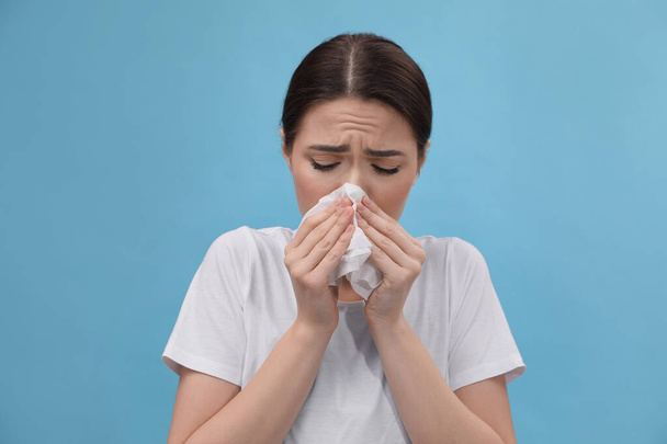 Woman blowing nose on light blue background. Cold symptoms - Фото, изображение