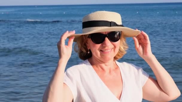 krásná 50 letá žena v slamáku a sluneční brýle na modrém mořském pozadí. Léto, dovolená, dovolená, aktivní důchodci - Záběry, video