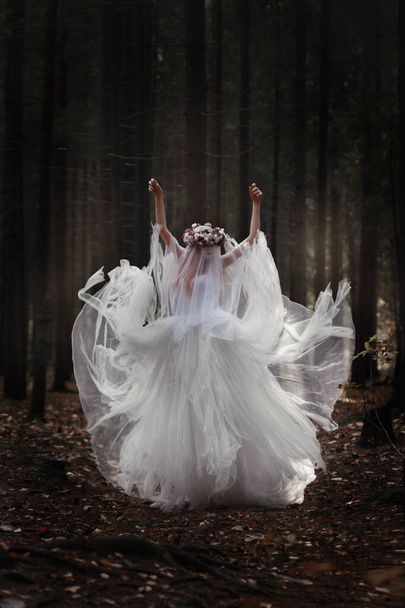 The girl the bride in a long white dress and a veil is dancing in a gloomy forest. - Foto, Imagen
