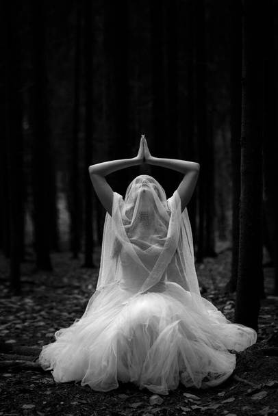 Black and white portrait of a mysterious woman bride in a gloomy forest in a prayer pose. - Photo, Image