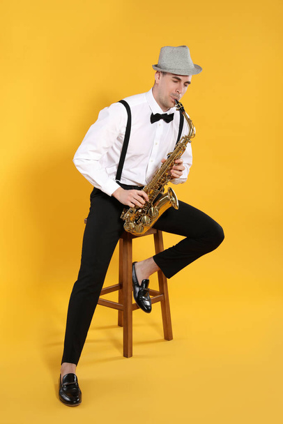 Young man in elegant outfit playing saxophone on yellow background - 写真・画像