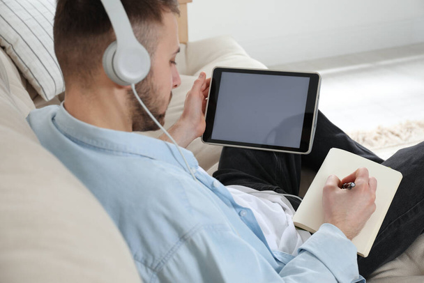 Young man with headphones using modern tablet for studying at home, closeup. Distance learning - Fotó, kép