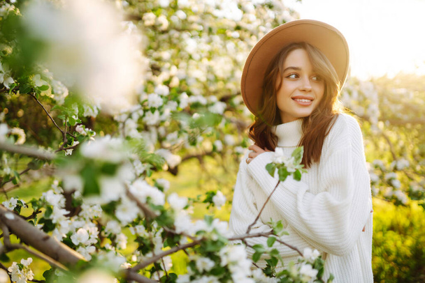 Young woman enjoying scent in blooming spring garden. The concept of relax, travel, freedom and spring vacation. Fashion style - Foto, afbeelding