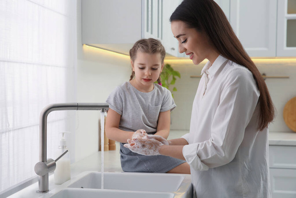 Mother and daughter washing hands with liquid soap in kitchen - Fotografie, Obrázek