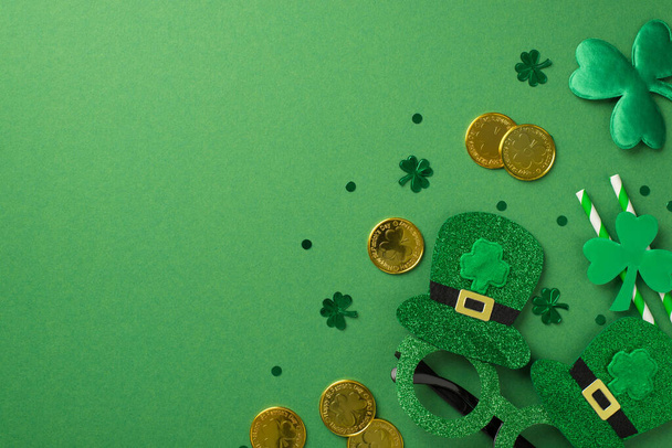 Вид сверху фото зеленых блестящих очков в шляпах две полосатые соломинки для напитков золотые монеты и много конфетти в виде клеверов и точек на зеленом изолированном фоне копирайта - Фото, изображение