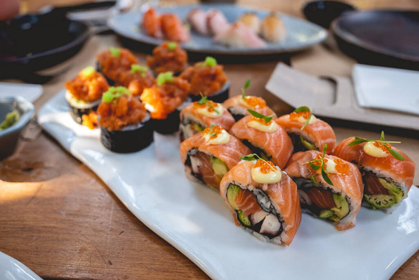 Az ínyenc sushi tekercsek közelsége lazaccal, masagóval (halikrákkal), avokádóval, polippal és norival fehér tálban - Fotó, kép