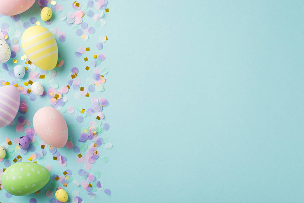 Visão superior foto de decorações de Páscoa ovos de páscoa multicoloridos ouro rosa e confete roxo em fundo azul pastel isolado com espaço vazio - Foto, Imagem