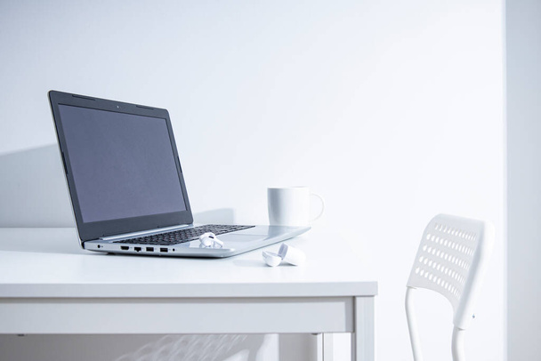 Laptopot, poharat, vezeték nélküli fejhallgatót egy fehér asztalon. Szabadúszó munkahelye  - Fotó, kép