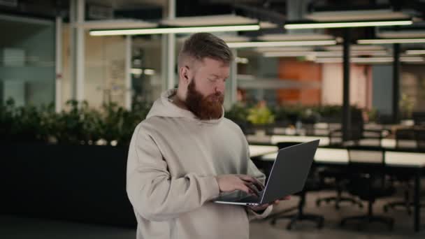 Hombre usando el ordenador portátil de trabajo en línea de pie en la oficina, Vista lateral - Imágenes, Vídeo