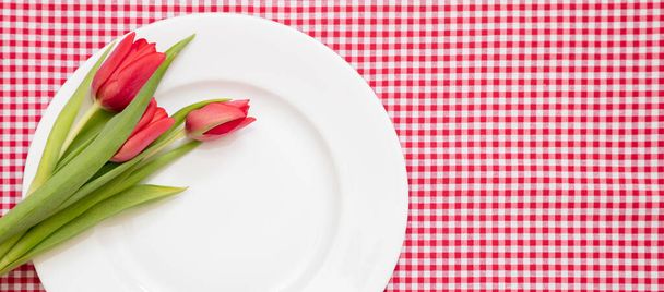 Kevätlomapöytä. Tuore punainen tulppaani kukka koristelu valkoinen levy, ruudullinen pöytäliina, ylhäältä - Valokuva, kuva