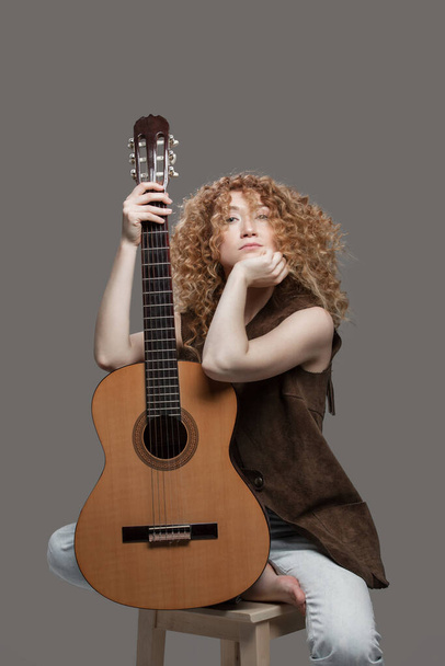 Een jonge vrouw met krullend haar en een gitaar. - Foto, afbeelding