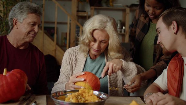  Grandmother tries to carefully cut off the top of the pumpkin and communicates with her grandson and husband - Photo, Image