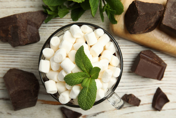 Glass cup of delicious hot chocolate with marshmallows and fresh mint on white wooden table flat lay - Foto, Imagen
