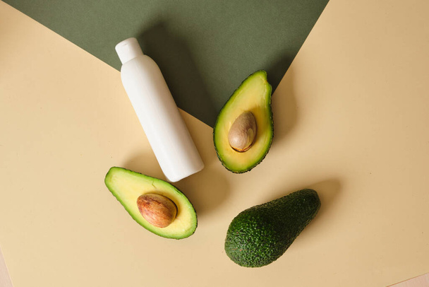 mock up white plastic bottle of cream with avocado slices on a green and beige background. Natural cosmetics concept. - Fotografie, Obrázek