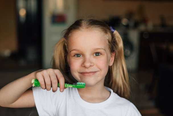 portrait of a child who brushes his teeth with a green toothbrush at home with a smile. Hygiene and health prevention of diseases of the teeth and oral cavity in children - Photo, image