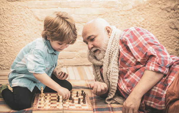 Grandfather playing chess with his grandson. Senior man teaching his grandson to play chess. Cute boy developing chess strategy. Chess competition. - Foto, Imagem