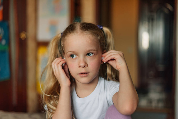 portrait of a smiling child, listening to music in white headphones, dancing, fooling around at home. beautiful girl listens to an audio fairy tale in headphones. generation alpha - Foto, imagen