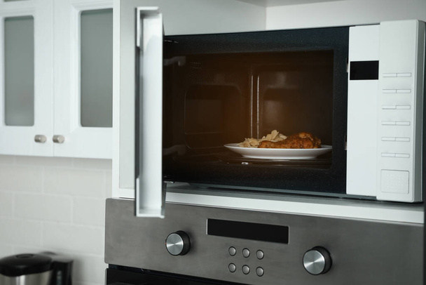 Open microwave oven with food on white shelf in kitchen - 写真・画像
