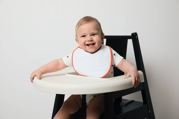 Lindo bebé vistiendo babero en trona sobre fondo blanco - Foto, Imagen