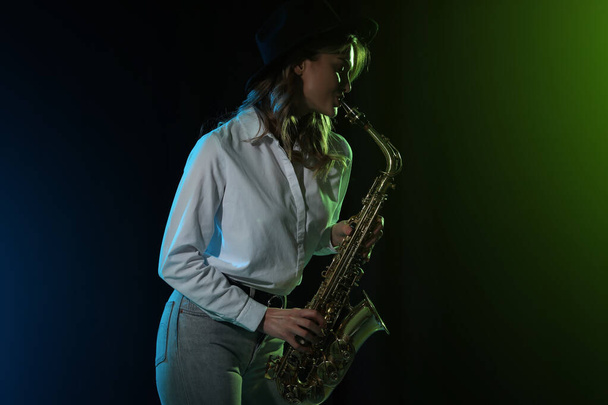 Beautiful young woman playing saxophone on dark background - Fotó, kép