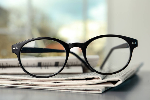 Stack of newspapers and glasses on grey table indoors, closeup - Fotografie, Obrázek