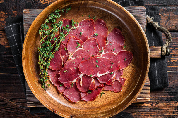 Pastrami slices, dried beef meat with herbs in wooden plate. Wooden background. Top view - Φωτογραφία, εικόνα