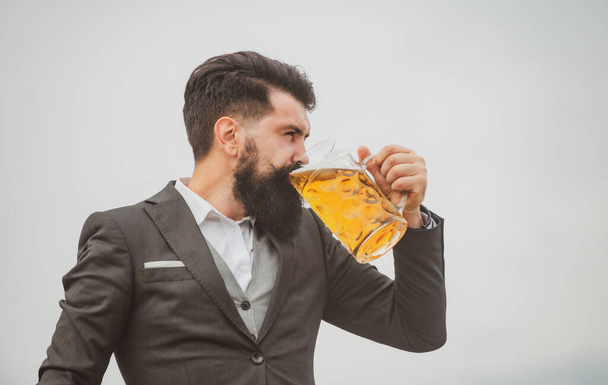 古典的なスーツを着た男がビールを飲む。ビールの大きなカップを持つ男の肖像. - 写真・画像