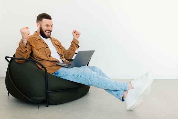 Joyful Freelancer Guy χρησιμοποιώντας φορητό υπολογιστή τρέμουν γροθιές κάθεται μέσα - Φωτογραφία, εικόνα