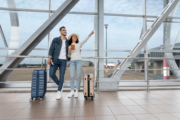 休暇の申し込み。空港で待っている楽しい若いアラブカップルの肖像 - 写真・画像
