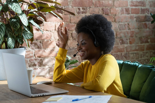 Sonriente empleada Afro mujer hablando en chat de vídeo con los clientes en el ordenador portátil, viendo webinar en casa - Foto, Imagen