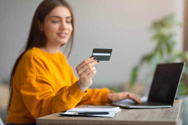 Boldog fiatal hölgy hitelkártyával távoli fizetés, online vásárlás laptopon keresztül, termékek vásárlása webáruházban otthon - Fotó, kép