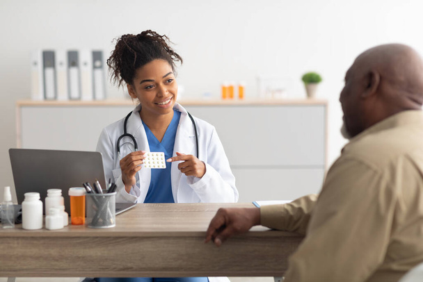 Опытный черный врач показывает таблетки пациенту мужского пола - Фото, изображение