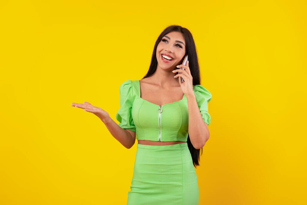 Alegre dama hablando por teléfono celular en el estudio amarillo - Foto, Imagen