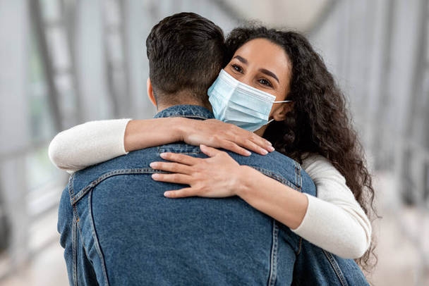 Счастливого воссоединения. Мужчина и женщина в медицинской маске, обнимающиеся в аэропорту, крупный план - Фото, изображение