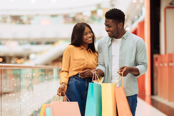 Happy black couple holding shopping bags looking at each other - Foto, afbeelding