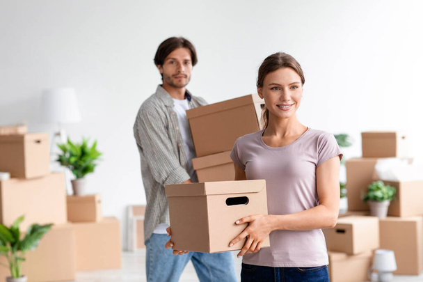 Smiling millennial caucasian male and female in casual enjoy moving, carry cardboard boxes with belongings - Photo, Image