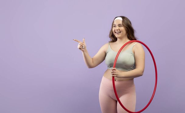 Tevreden enthousiast plus size europese jonge vrouw in sportkleding met open mond met hula hoepel - Foto, afbeelding