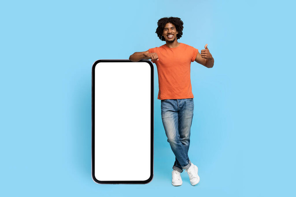 Positivo afroamericano posando con teléfono inteligente con pantalla en blanco - Foto, Imagen