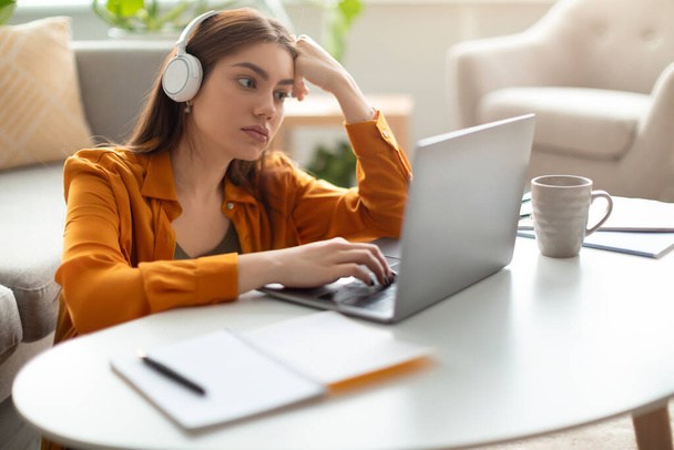 Vakava nuori nainen kannettavan tietokoneen kuulokkeet, työskentely tai opiskelu verkossa, ottaa video chat kotona toimistossa - Valokuva, kuva