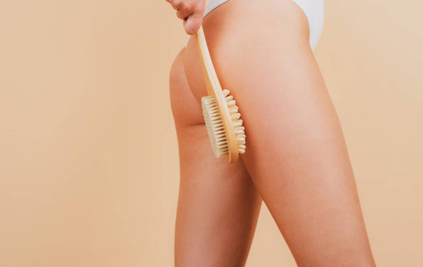 Woman makes massage with a wooden soft massage brush for body. Woman legs and buttocks ass without cellulite. Skin treatment. Anti-cellulite body massage for leg and butt. Spa and wellness. - Foto, Imagem