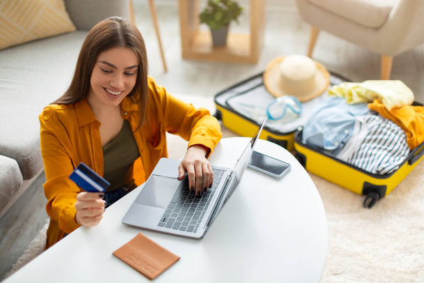 Mujer joven feliz con tarjeta de crédito reserva de vacaciones en la agencia de viajes o hacer la reserva de hotel en línea, utilizando el ordenador portátil - Foto, imagen
