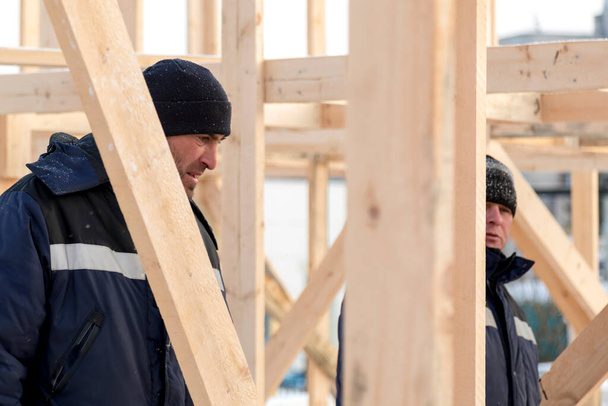 Строители в голубых куртках с капюшонами на установке деревянной горки - Фото, изображение