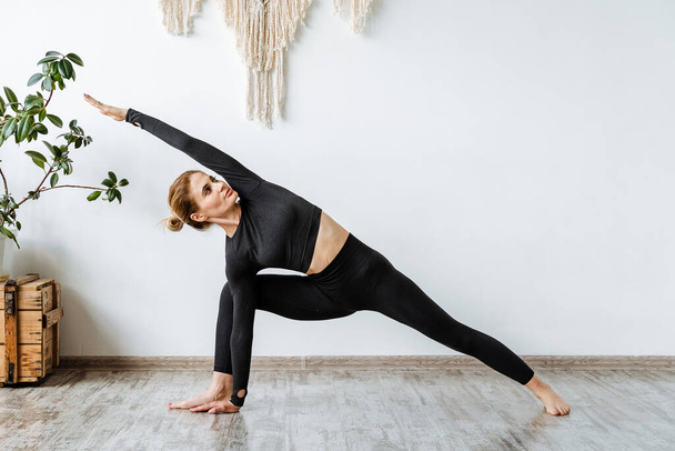 Portrait of a girl practicing yoga in a black suit.One of the main poses in yoga, the pose of a warrior.Virasana.Zen.Development of rolling stock and ankles. High quality photo - Foto, Imagen