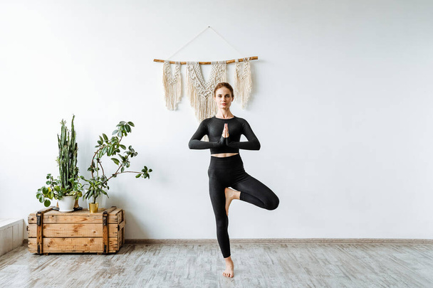 Girl practices yoga in a bright studio. The instructor builds Tree Pose. Vrikshasana. to find harmony and tranquility in our world. Zen. High quality photo - 写真・画像