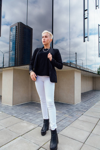 Young stylish business woman with short hair and nose piercing. Confident girl look like lesbian standing near business center with mirror walls - Фото, изображение