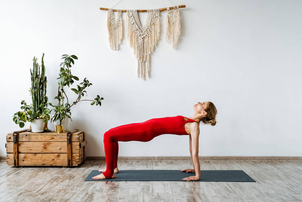 A girl yoga instructor stands for the pose of an upside-down table. Sahaja Purvottanasana.Yoga classes in a bright, cozy room. Bright training suit. High quality photo - Zdjęcie, obraz